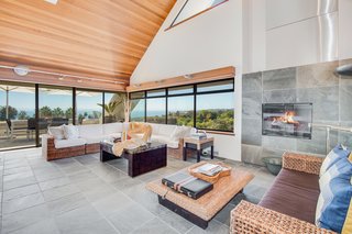 Windows wrap the corner of the home, providing continuous views from the hills to the ocean. The slate flooring extends upwards to wrap the fireplace.