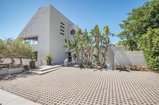 The white concrete exterior of the triangular home is enclosed by lush vegetation. A courtyard welcomes guests upon entry.