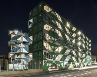 Large cuts in the outer walls of the shipping containers create a geometric pattern of glazed openings. At night, the openings create a patterned facade that is both solid and transparent.