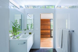 Simple, white tile extends from floor-to-ceiling in the bathroom. A clerestory window draws in daylight, further reflecting off the glossy surfaces to create a light-filled interior space.