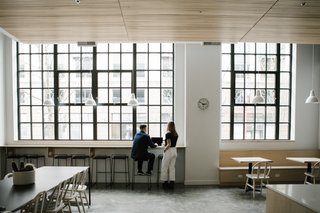 Large, black-framed windows maintain the original character of the building while drawing in natural lighting. A custom built-in ledge and banquette provide alternative working seating in a collaborative environment.