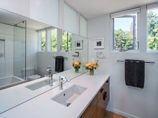 In the bathroom, a floating wood vanity adds a simple modern touch. A large, seamless mirror and windows allow daylight to fill this small space.