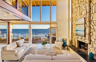 The two-story living space is open to the bedrooms above.  A full-height wall of windows draws the ocean views inwards. 