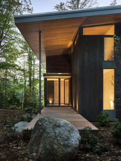 The exterior palette consists of dark cedar siding, mahogany decks, and exposed gray steel beams. 