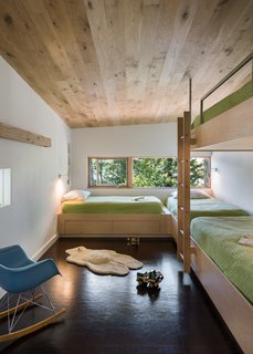 Custom, built-in bunk beds were constructed out of Baltic birch plywood, which stand out against the dark cork floors. Each bed includes a sconce for reading, along with built-in storage. In the bunk room, a sliding partition that opens to the adjacent catwalk adds a sense of whimsy. 