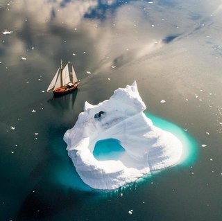 Sailboat creeping along the edge of an iceberg in Greenlands Sermilik Fjord.