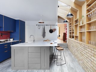 The center island serves as a breakfast nook, sink space, and storage, and marks a transition from bold, blue cabinets into open shelving.