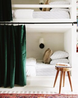 The kids' bedroom features a fitted Bahama sheet and duvet from Wayfair, a deer pillow from the Pillow Cover Store on Etsy, insulated velvet curtains from Amazon, a single Ink + Ivy Arcadia natural dining stool as a nightstand, an Arc midcentury sconce from West Elm, and a cozy Safavieh Corinth Rug from Target. 