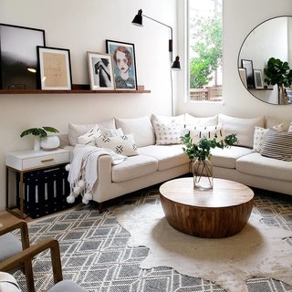 A Sloane Interior Define sofa wraps around the living room with a Jacob coffee table from Wayfair in the center. The Acme Coleen side table in white and brass is from Houzz, and a Talari indigo ottoman from The Citizenry is stashed underneath. Expanding the space is a Glen mirror from Modern Komfort.