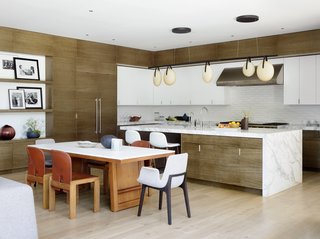 A generously sized chef's kitchen fits seamlessly with the contemporary lines of the home. A Rich Brilliant Willing Gala light is suspended above a Pietra Fina island. The backsplash features Heath Diamond tiles in Chalk-2. The dining table comprises a McGuire Furniture Company walnut base with a Staron top, and is surrounded by vintage Cassina and Poliform Ventura chairs. 