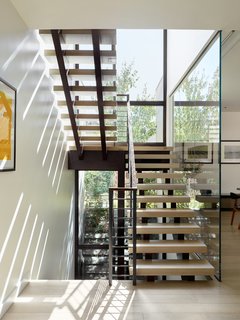 An open, central stair located next to a floor-to-ceiling glass wall offers another moment of connection with the outdoors.