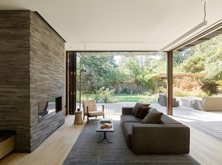 Accordion doors open up to join interior and exterior spaces. Inside, the Andy Sofa by B&B Italia and Capo lounge chair by Neri & Hu for De La Espada offer cozy seating beside the Island Stone Temple Lava fireplace. An Imari rug by Restoration Hardware and a vintage coffee table ground the room.