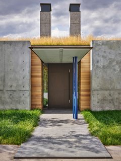 A break in the concrete facade reveals the front entrance, which is marked by a thin steel canopy and two chimneys.