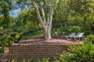 Tucked away from the street is a side yard that travels up behind the home to a flat viewing terrace, shaded beneath a large tree. 