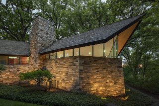 The one-story home is topped with an asymmetrical gable cedar shingle roof with cantilevered gable ends, deep overhangs, and pronounced redwood fascia boards.