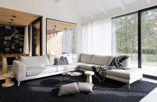 Full-height glazing fills the living room with natural light. The Scandinavian-inspired space is furnished with items like the B&B Italia Fat-Fat table and Vitra Cork Family stools.