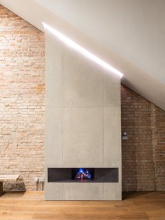 The concrete fireplace draws attention to the sloped ceiling, as well as to the unique lighting feature above.