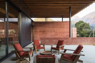 The veranda on the southwest side of the home is shielded from the elements by the roof. The chairs upholstered in red fabric match the pigmented concrete walls.