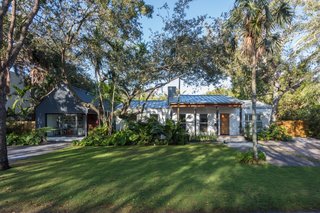 The home is nestled in a lushly planted landscape with tropical flora and live oaks.