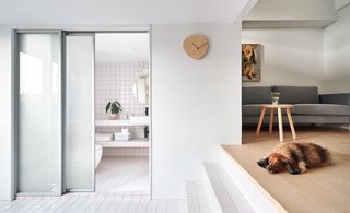 An opaque sliding glass door separates the bathroom from the dining area. White tile with pink-colored grout ties the two spaces together.