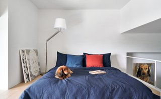 The bed, partially tucked behind a wall, is bathed in natural light from a large window.