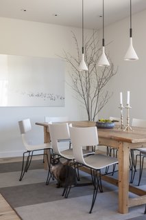 Aplomb Suspension Lamps hang above the dining table, which is set above a custom area rug by the client's interior design firm. Sally, one of the cats, is seen here.