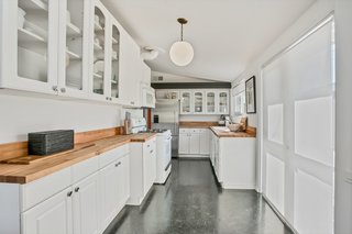 Beautiful butcher-block countertops lend a sense of warmth to the all-white kitchen with modern fixtures.