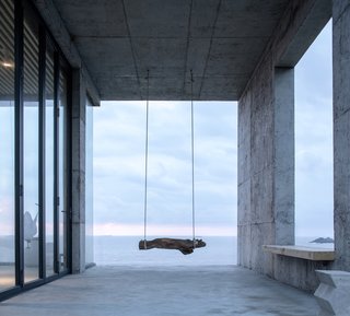 A swing, fashioned from string and driftwood, hangs from the ceiling of new the concrete addition.