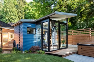 Blue-painted cedar siding wraps around the 169-square-foot Backyard Reading Retreat. The smaller wooden shed hidden in the rear houses a prefab dry sauna.