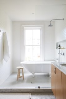 A clawfoot tub was installed beneath the window and can be seen from the bedroom. The semi-enclosed shower room is lined in white subway tile while sage green penny tiles cover the floors.