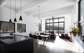 The minimalist interiors feature a mainly monochromatic palette with white walls and black surfaces, including the granite island top and window trim. Small pops of color help break up the color scheme.