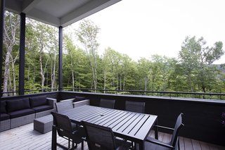 Untreated-timber floor planks provide contrast against the black-painted elements and furnishings in the covered patio.