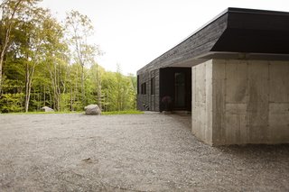 The covered parking pad is supported by an exposed concrete volume with (unseen) built-in storage. The concrete also provides protection against water runoff from the mountain.