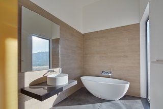The guest bedroom features a soaking tub with a full-height window overlooking the deck and landscape beyond.