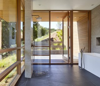 Shielded from the sun by large overhangs, the master bath is wrapped in full-height glazing. The porcelain tile floors are from Porcelanosa, and the walls are a mix of Western Red Cedar, tile, and painted gypsum.