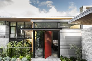 A bright-red pivot door marks the main entrance, located a half-level below the upper floor.
