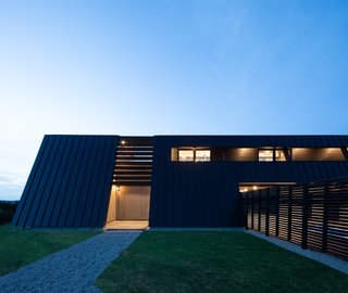 A glimpse of the entrance at dusk from the south elevation. To the right is a swimming pool shielded behind wooden fencing.