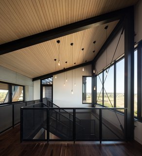 Walnut flooring has been used throughout the light-filled home. Here, a bridge connects the living spaces to the exterior deck and staircase.