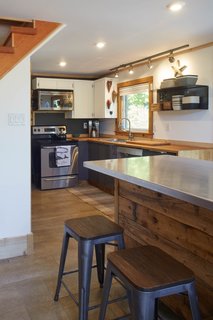 The kitchen was revamped with new modern appliances, including a dishwasher. The custom kitchen island was built from two IKEA cabinets on wheels, topped with an aluminum countertop, and wrapped in salvaged cedar-fence panels.
