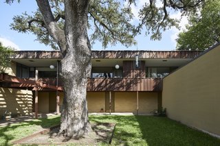 A massive oak tree is the focal point of the entry courtyard. The entrances to each unit are sheltered beneath the overhanging second-story balcony. 