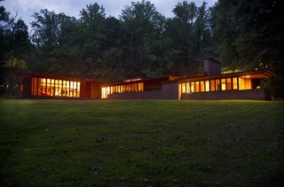 A nighttime view of the home seen from the northeast. To the right is the bedroom wing extending north. To the left is the living room wing stretching to the east.