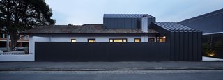 A long fence built from Colorbond standing-seam metal panels shields the home from the busy street.
