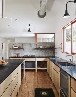 The cast-in-place concrete site wall that pierces the volume frames the entry and serves as the kitchen backsplash. The kitchen appliances are by Fisher & Paykel.