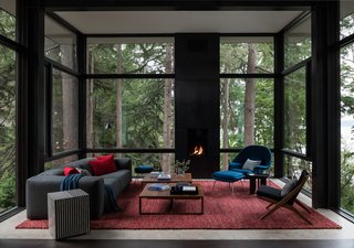 Enclosed in glass and elevated in the tree canopy, the living room is furnished with midcentury modern classics including a Case Kelston sofa from DWR and a Knoll Womb chair and ottoman. The custom red wool rug is from Driscoll Robbins.