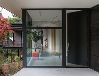 An oversized entrance door leads to an angled hallway that obscures views to create an element of surprise. The Vollen bench in Custom Red Lacquer is from Chadhaus.