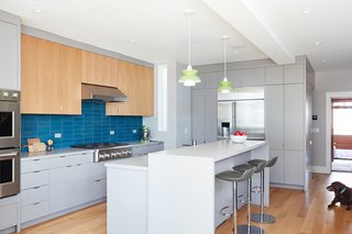 The light-filled kitchen features Leo Bar stools from Room and Board, Doo-Wop pendant lights by Louis Poulsen, and GE Monogram appliances. The backsplash is Heath Tile and the countertops are Solid Surface.