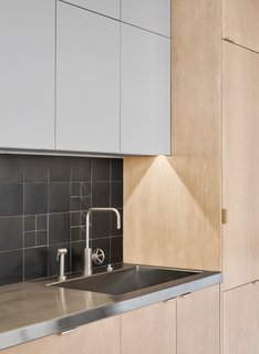 A backsplash featuring custom matte black ceramic tiles by Waterworks is paired with stainless steel countertops. The timber cabinets, by JRs Custom Cabinets, are made of white oak.