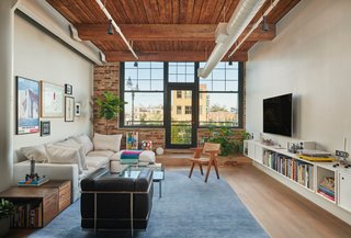 The light-filled living area includes a Le Corbusier leather chair and a caned lounge chair. A door on the far wall opens up to a balcony space.