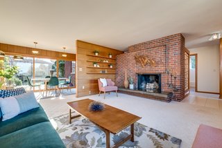 A timber curtain wall with floating shelves divides the living room from the kitchen and dining areas.
