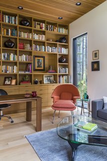 The cozy study is furnished with custom timber shelving, a Gus Modern Jane sectional, a Womb chair, an ottoman designed by Eero Saarinen for Knoll, and a Noguchi table.